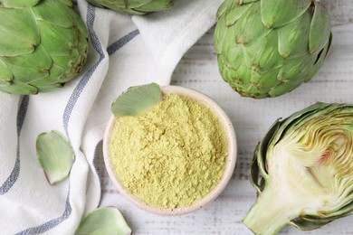 Bowl with powder and fresh artichokes on white wooden table, flat lay