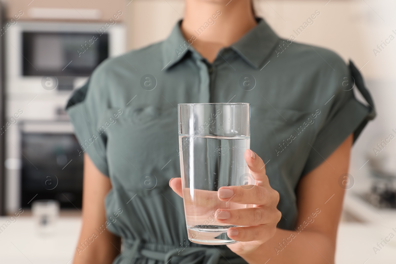 Photo of Woman holding glass with pure water in kitchen, closeup