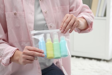 Photo of Woman holding plastic bag of cosmetic travel kit indoors, closeup and space for text. Bath accessories