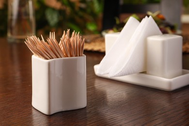 Holder with many toothpicks on wooden table, closeup. Space for text