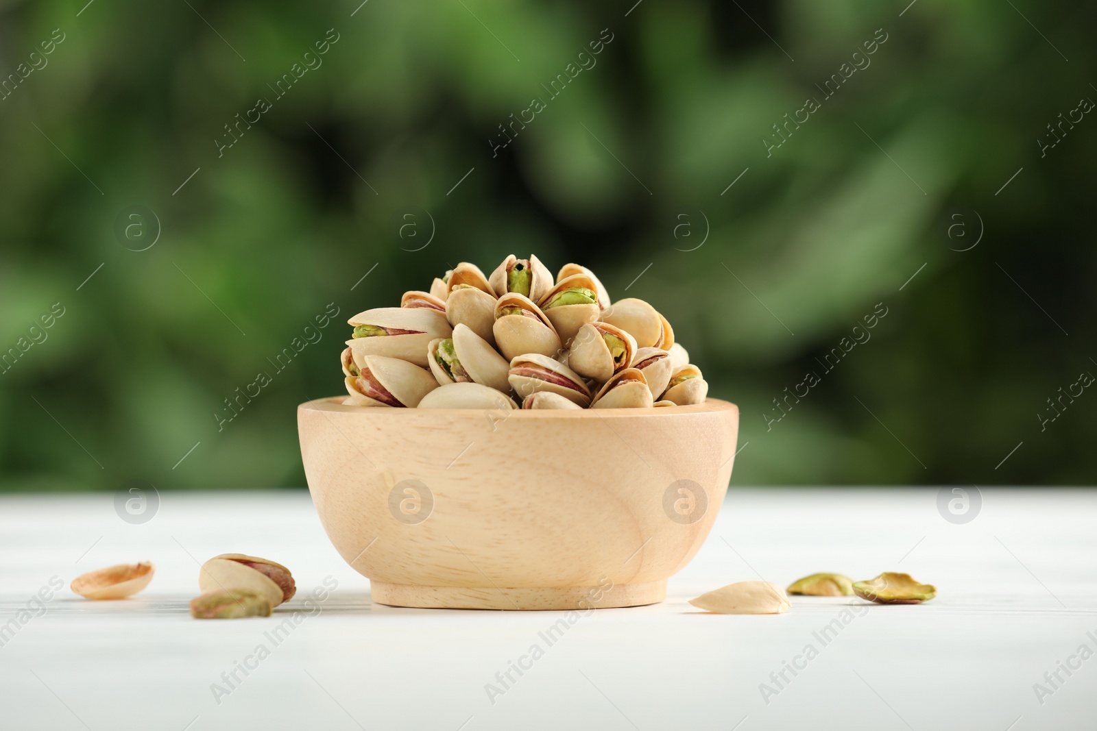 Photo of Tasty pistachios in bowl on white wooden table against blurred background, closeup