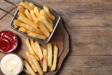 Photo of Tasty French fries served with sauces on wooden table, top view. Space for text