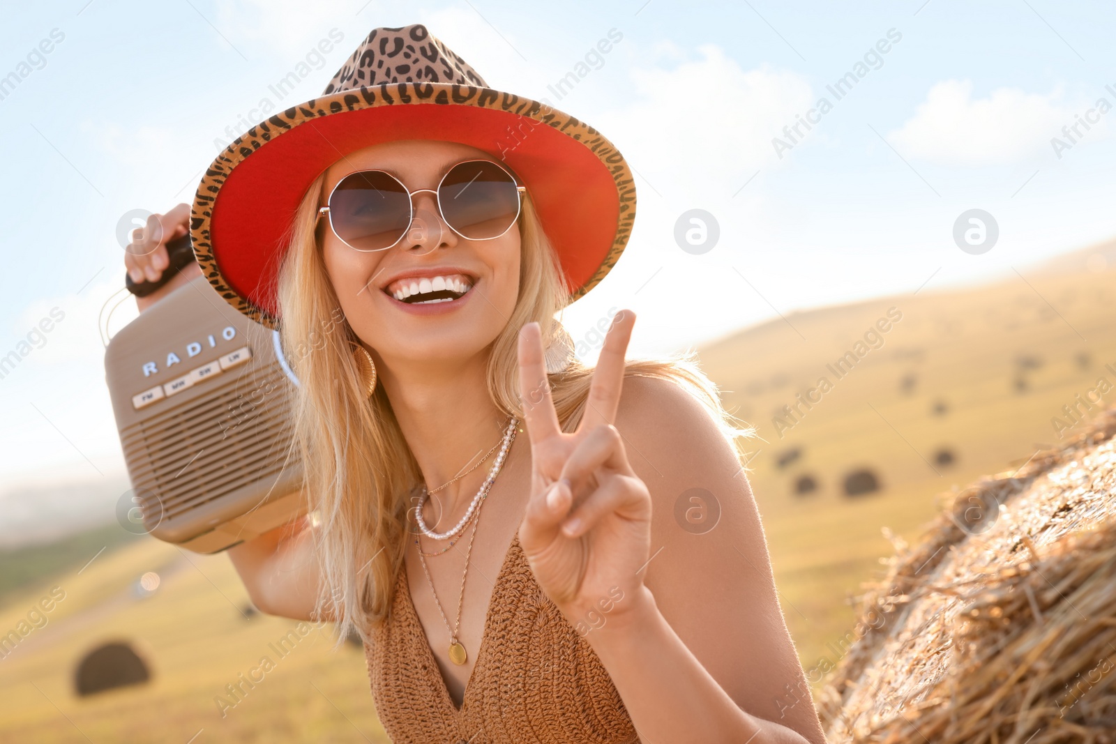 Photo of Happy hippie woman with radio receiver showing peace sign in field