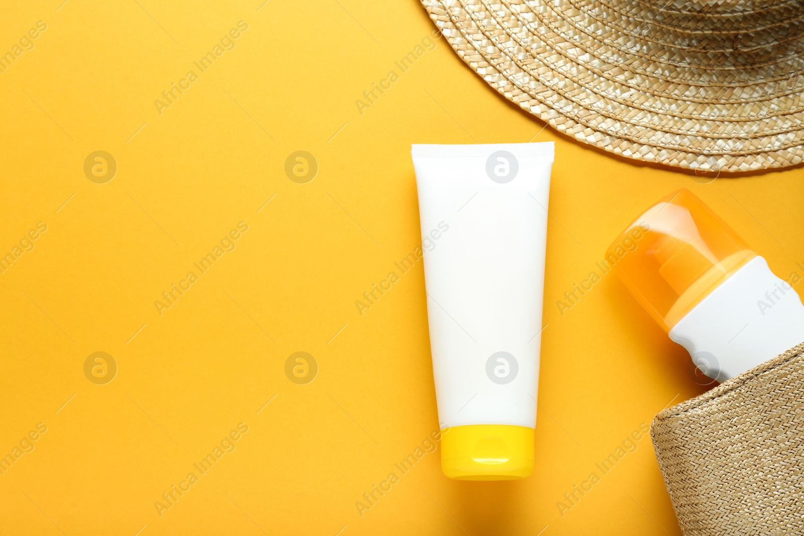 Photo of Suntan products and wicker hat on orange background, flat lay. Space for text