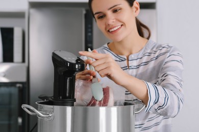 Photo of Woman putting vacuum packed meat into pot and using thermal immersion circulator indoors, focus on hand. Sous vide cooking