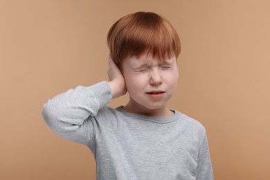 Photo of Hearing problem. Little boy suffering from ear pain on pale brown background