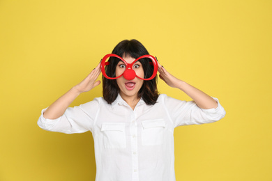 Photo of Funny woman with clown nose and large glasses on yellow background. April fool's day