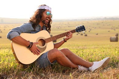 Handsome happy hippie man playing guitar in field