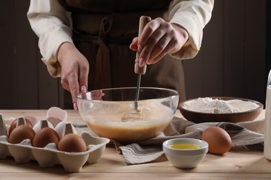 Woman making dough with whisk in bowl at table, closeup