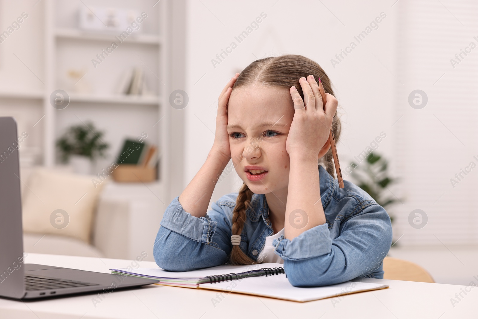 Photo of Little girl suffering from headache while doing homework at home