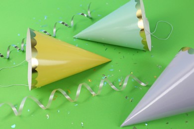 Photo of Bright party hats, serpentine streamers and confetti on green background