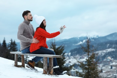 Couple sitting on bench and enjoying mountain landscape, space for text. Winter vacation