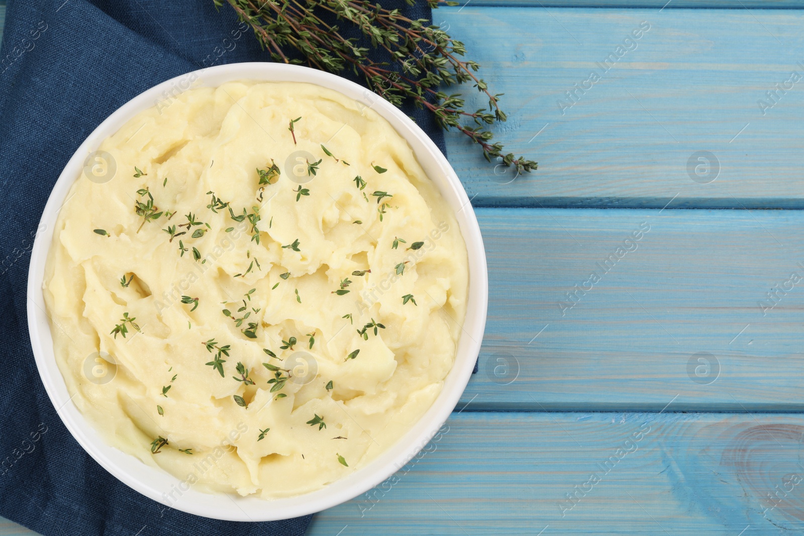 Photo of Bowl of tasty mashed potato with rosemary on light blue wooden table, flat lay. Space for text