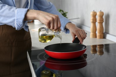 Photo of Vegetable fats. Woman pouring cooking oil into frying pan on stove in kitchen, closeup