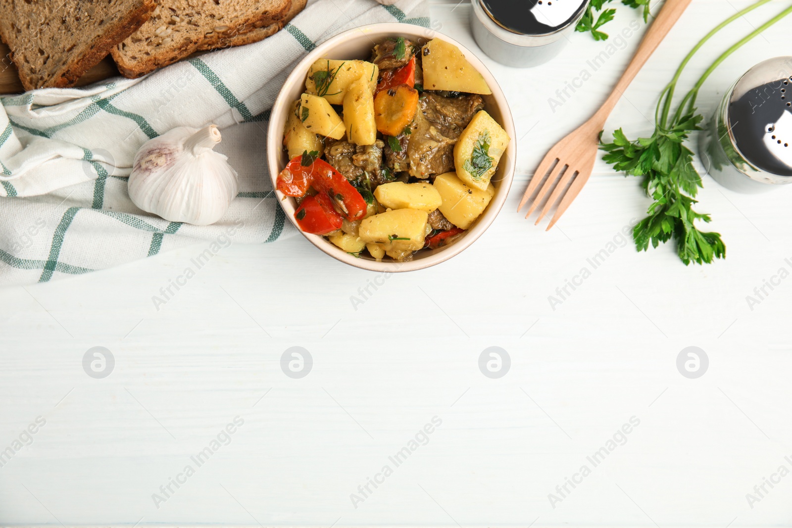 Photo of Tasty cooked dish with potatoes in earthenware served on white wooden table, flat lay. Space for text