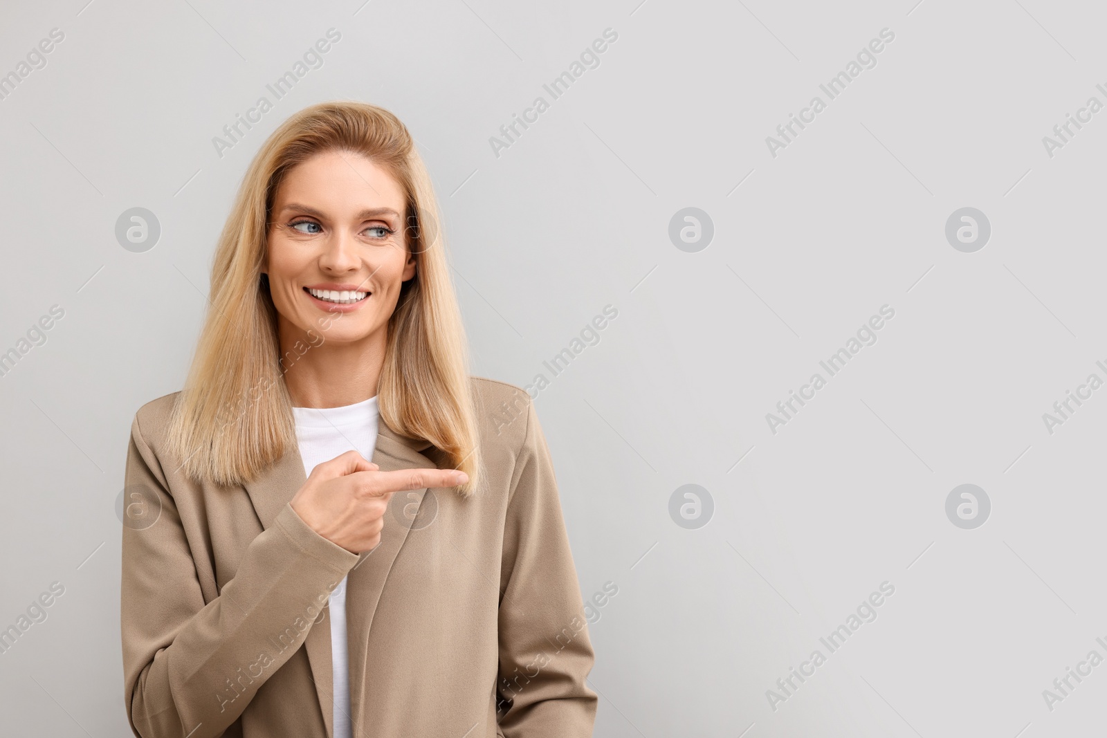 Photo of Portrait of smiling middle aged businesswoman pointing at something on light grey background. Space for text