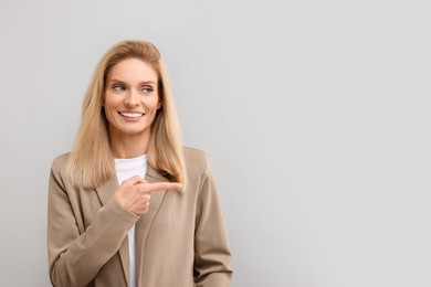 Portrait of smiling middle aged businesswoman pointing at something on light grey background. Space for text