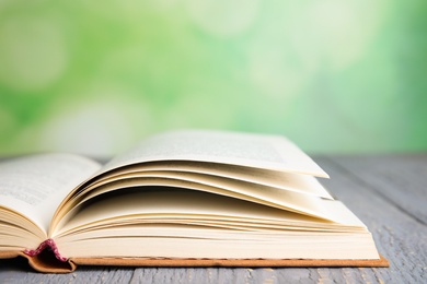 Photo of Open book on grey wooden table against blurred green background, closeup. Space for text