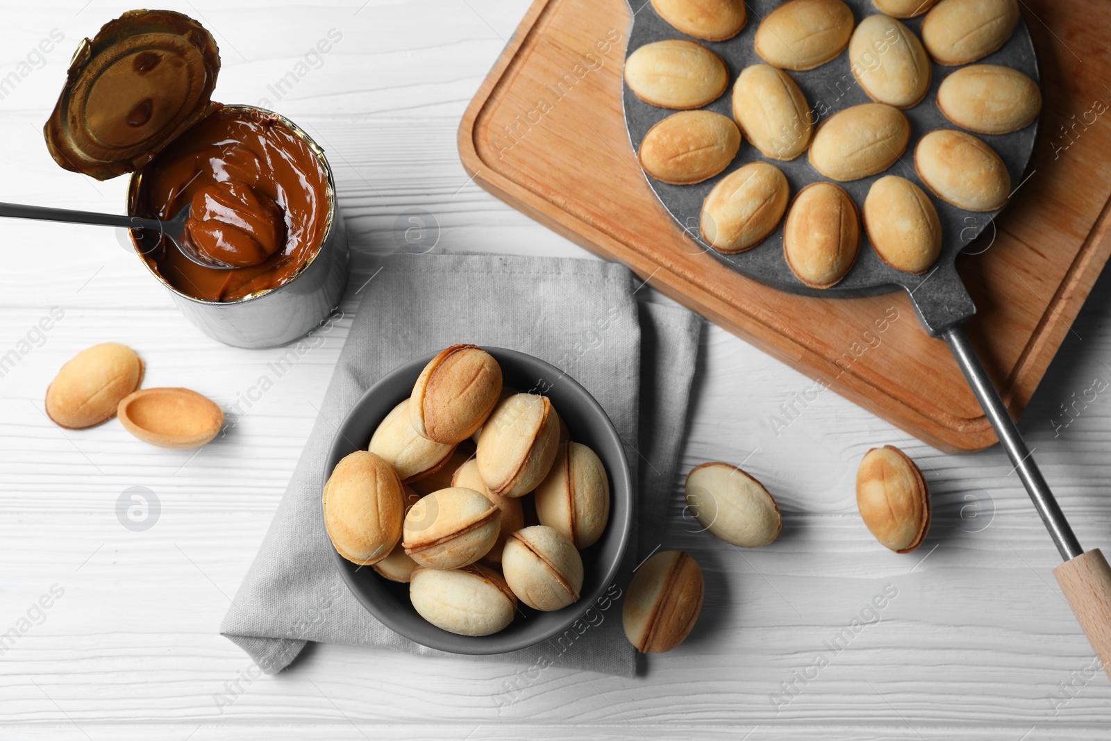 Photo of Delicious walnut shaped cookies with condensed milk on white wooden table, flat lay