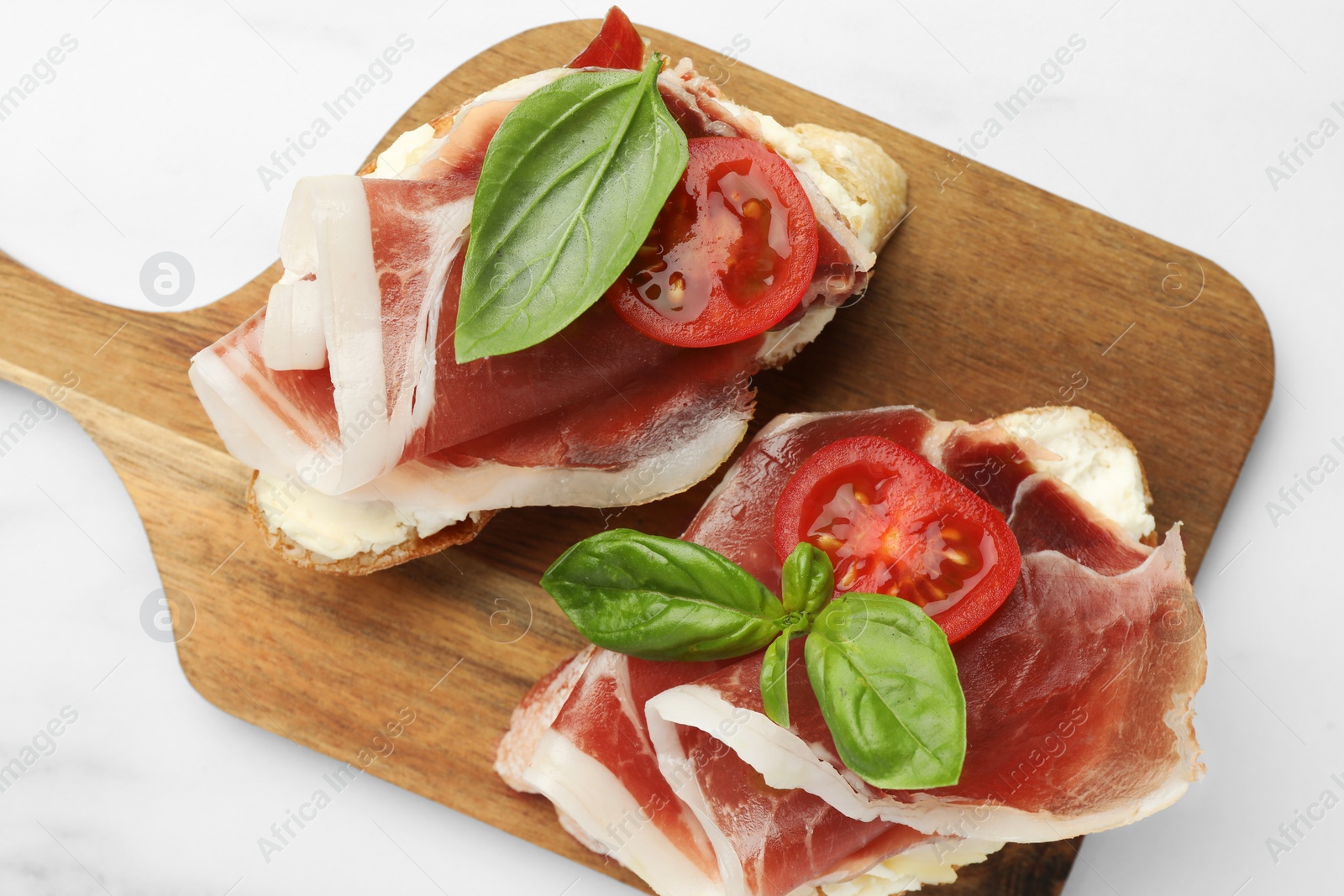 Photo of Tasty sandwiches with cured ham, basil and tomatoes on white marble table, top view