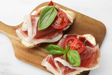 Tasty sandwiches with cured ham, basil and tomatoes on white marble table, top view
