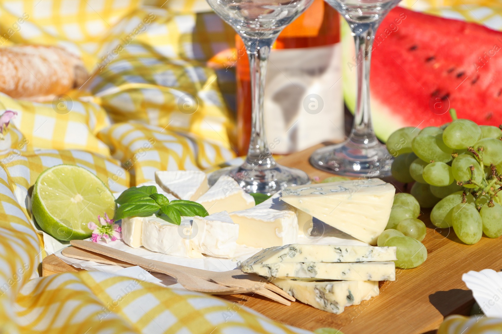 Photo of Delicious cheeses with basil and fruits on picnic blanket, closeup