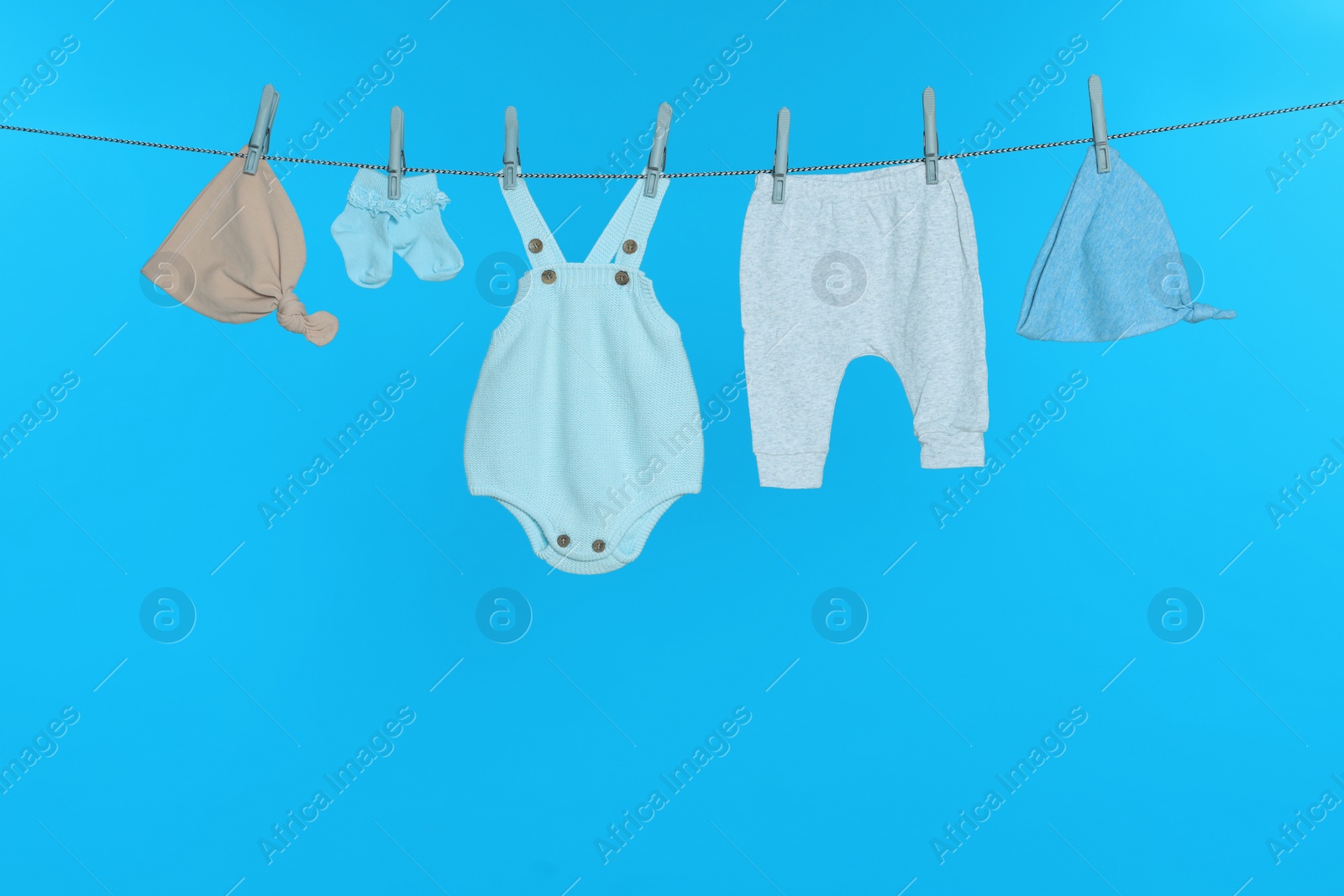 Photo of Different baby clothes drying on laundry line against light blue background