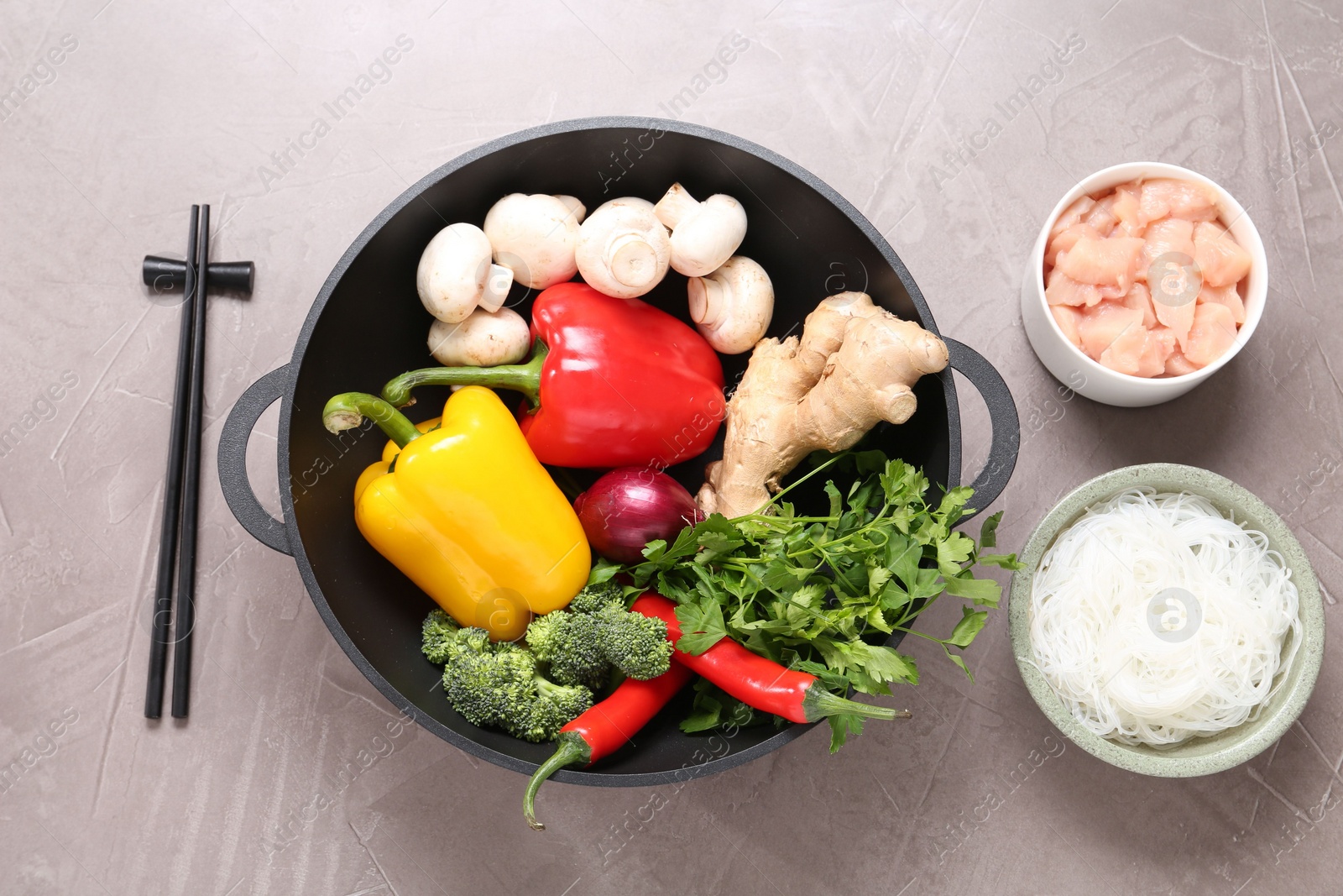 Photo of Wok, chopsticks and different products on grey textured table, flat lay