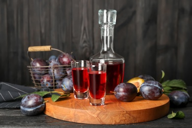 Delicious plum liquor and ripe fruits on black wooden table. Homemade strong alcoholic beverage