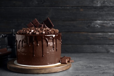 Photo of Freshly made delicious chocolate cake on grey table against black background. Space for text