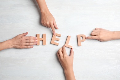 Photo of People making word "HELP" of letters on light background, top view