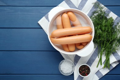 Photo of Bowl of delicious sausages, dill, pepper and salt on blue wooden table, flat lay. Space for text