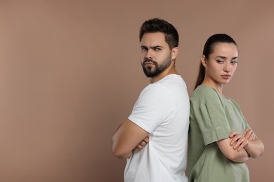 Resentful couple with crossed arms on brown background, space for text