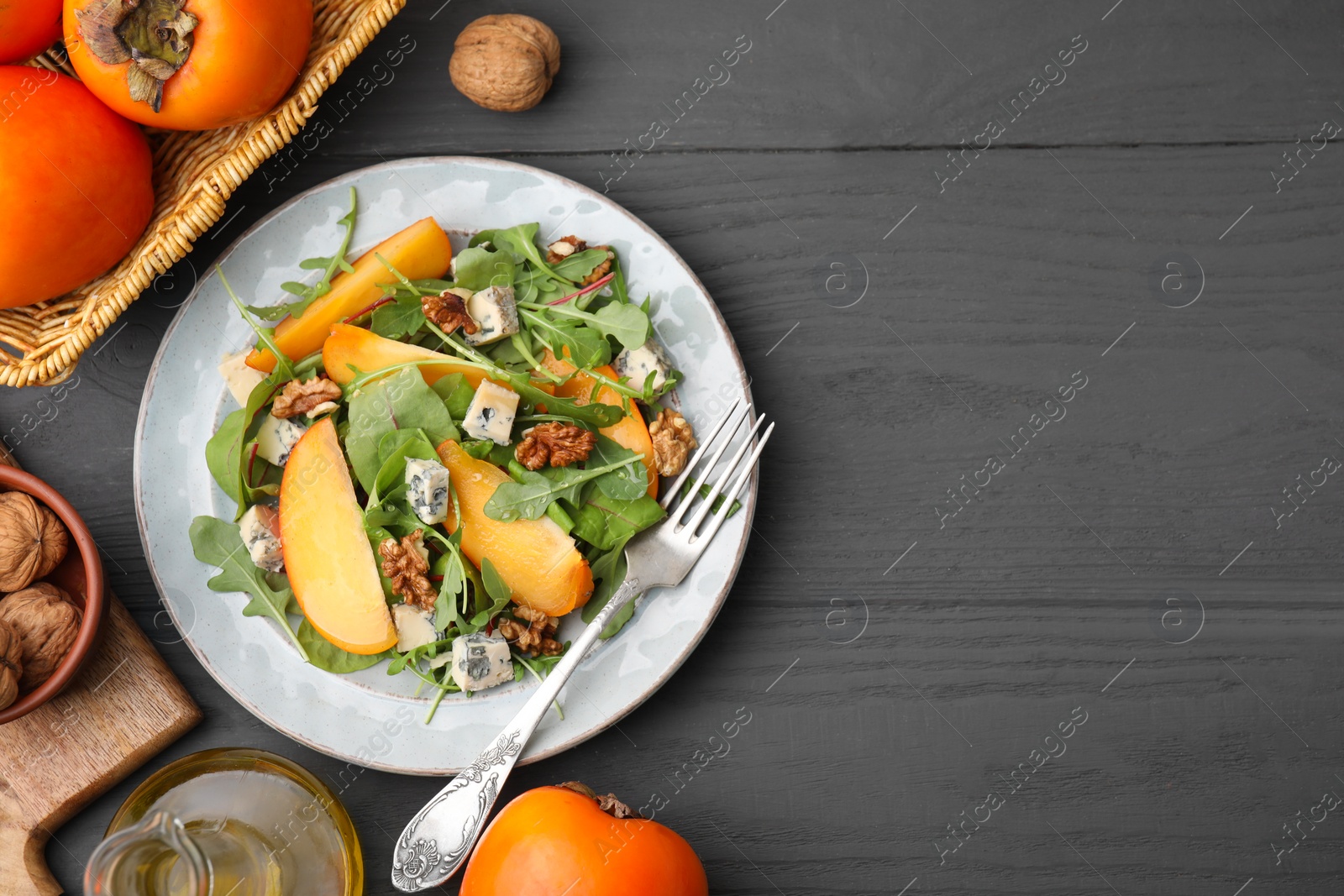 Photo of Tasty salad with persimmon, blue cheese and walnuts served on grey wooden table, flat lay. Space for text