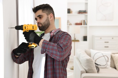 Photo of Young handyman working with electric drill at home