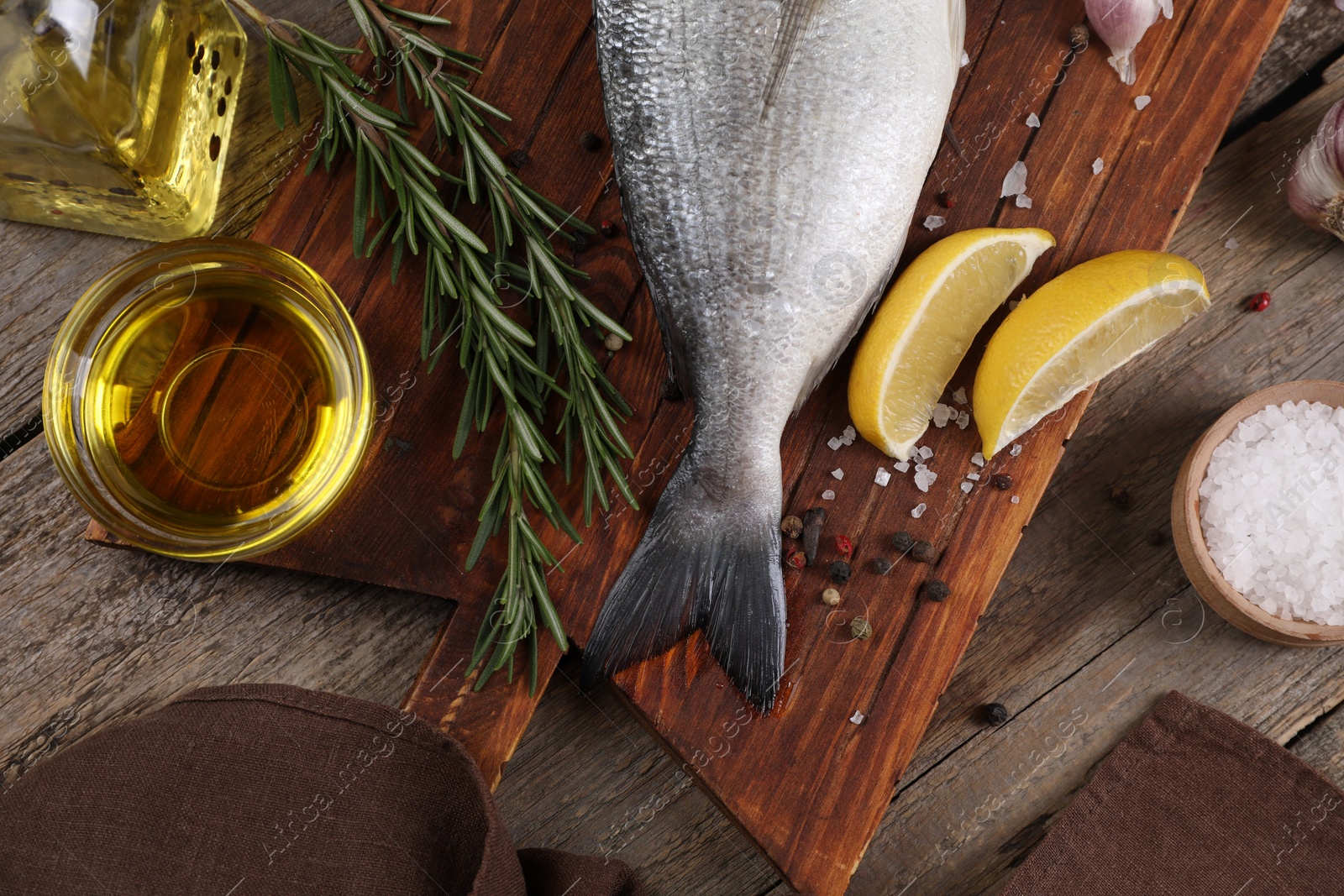 Photo of Raw dorado fish, lemon wedges, spices and oil on wooden table, flat lay