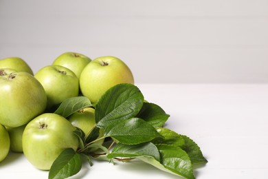 Photo of Fresh ripe green apples with leaves on white wooden table. Space for text