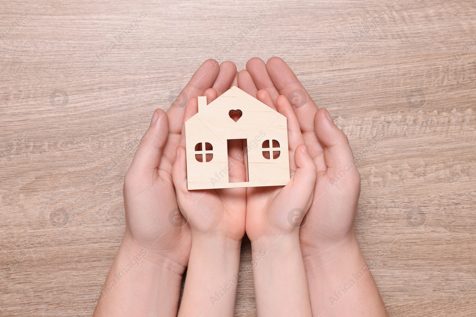 Photo of Home security concept. Man with his little child holding house model at wooden table, top view