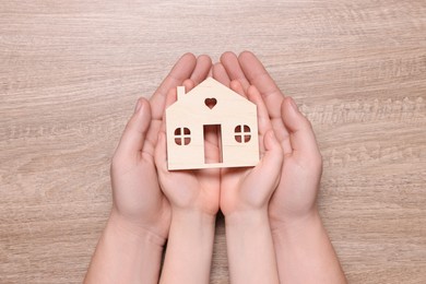 Home security concept. Man with his little child holding house model at wooden table, top view