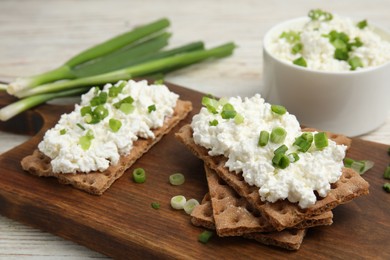 Crispy crackers with cottage cheese and green onion on white table, closeup