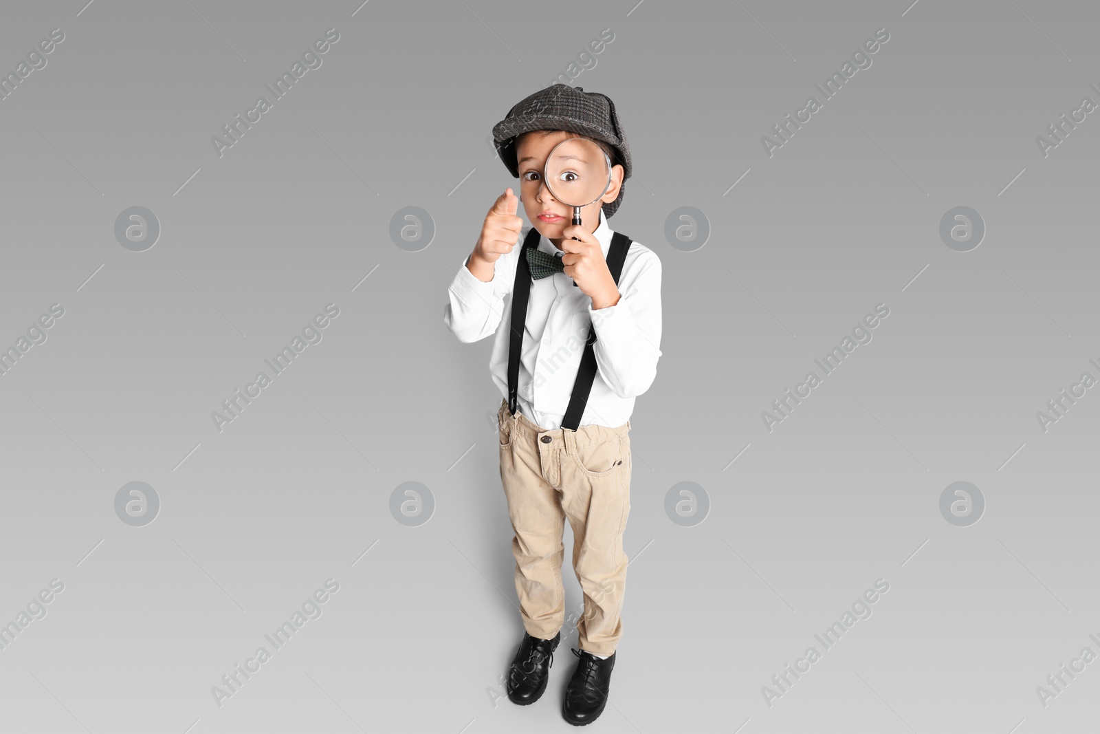 Photo of Little boy with magnifying glass playing detective on grey background