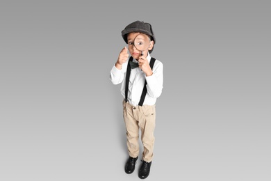 Photo of Little boy with magnifying glass playing detective on grey background