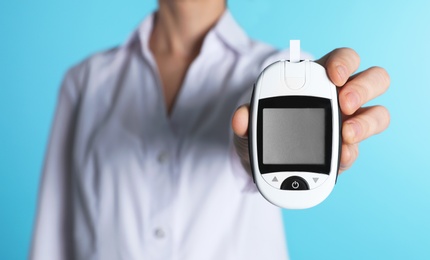 Photo of Female doctor holding digital glucometer on color background, closeup. Medical object