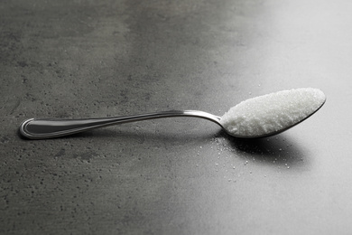 Photo of Spoon of white sugar on grey table