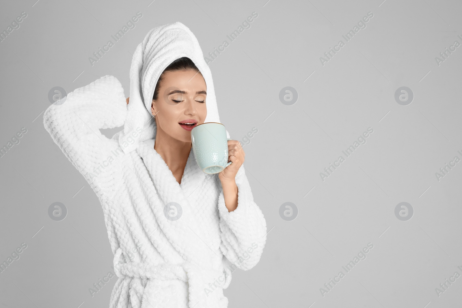 Photo of Beautiful young woman in bathrobe with cup of coffee on light grey background. Space for text