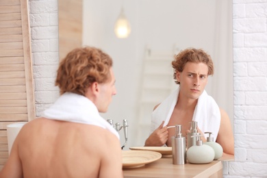 Young man looking in mirror after shaving at home