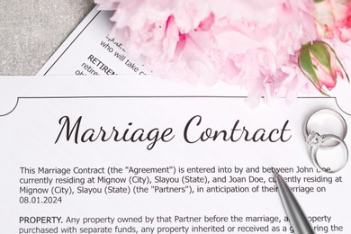 Marriage contract, wedding rings, pen and flowers on grey table, top view