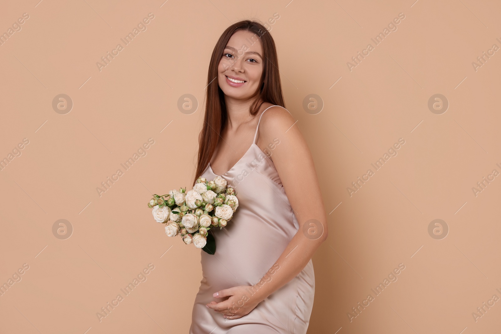 Photo of Beautiful pregnant woman in dress with bouquet of roses on beige background