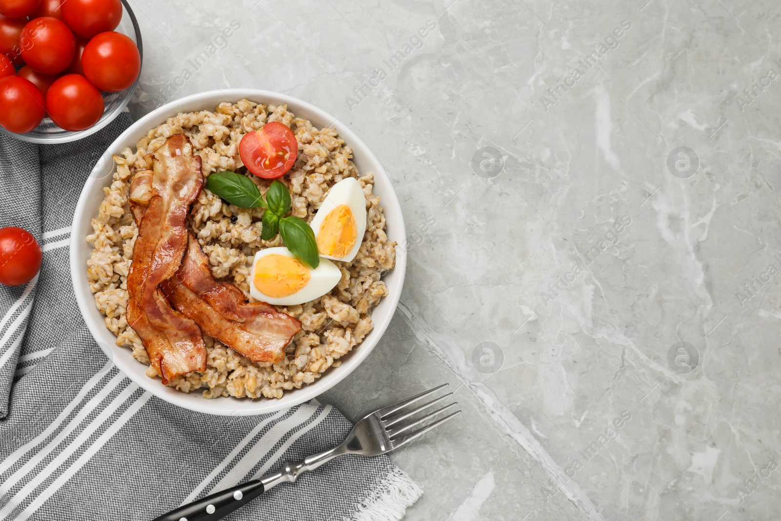 Photo of Tasty boiled oatmeal with egg, bacon and tomatoes served on light grey table, flat lay. Space for text