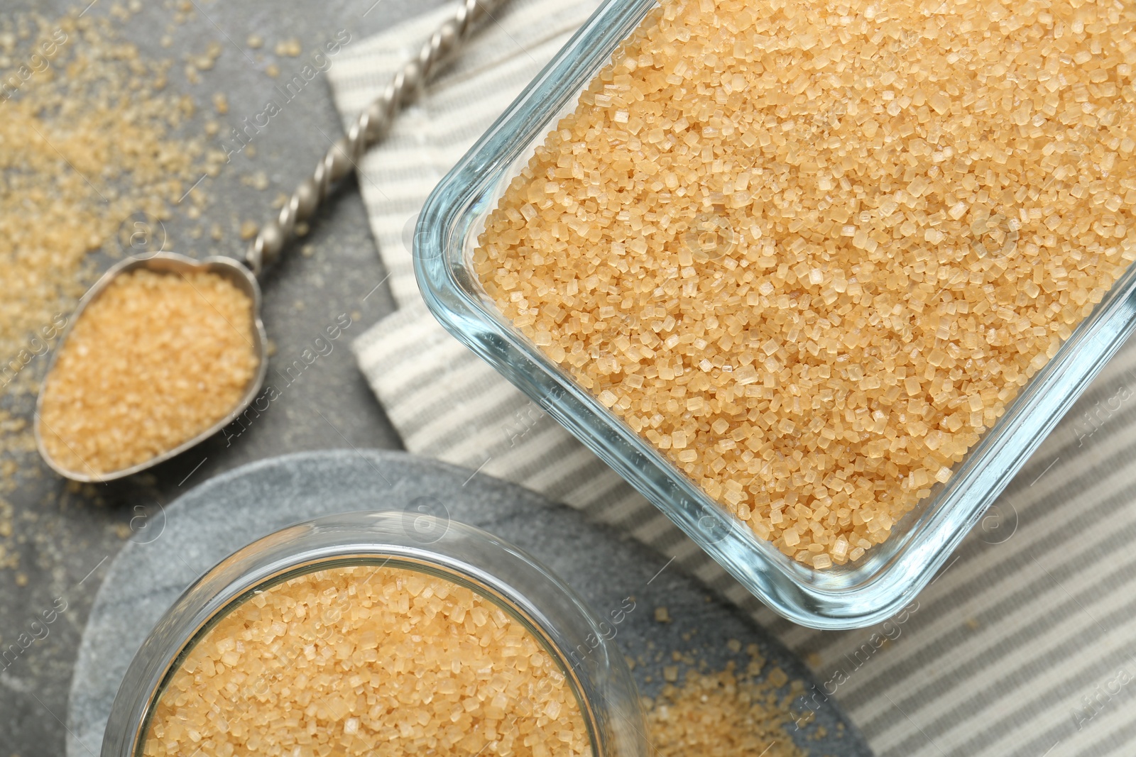 Photo of Brown sugar and spoon on grey table, flat lay